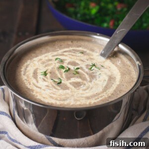 Mushroom soup in a pot with cream drizzled on top of it.