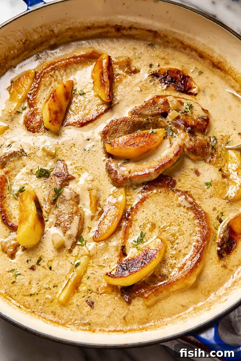 Tender boneless pork chops and apples nestled in a creamy apple cider sauce in a cast iron skillet, ready to be served