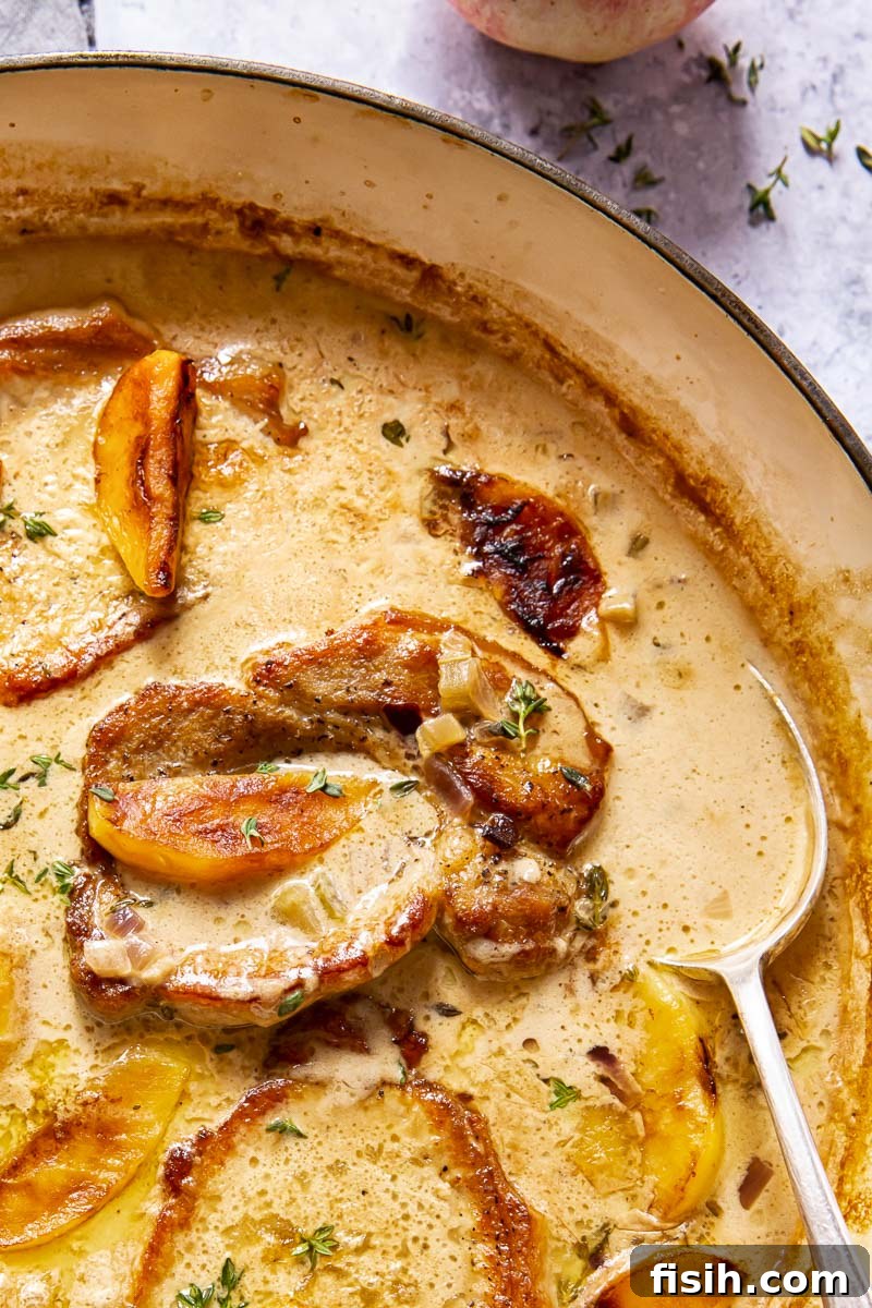 Boneless Pork Loin Steaks simmering in a creamy apple cider sauce, adorned with fresh apple slices