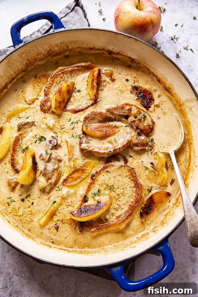 Close-up of boneless pork chops with apples and creamy sauce in a rustic serving dish, garnished with fresh thyme