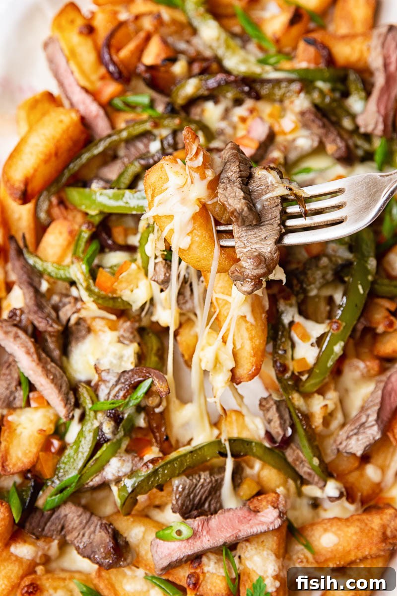 Smothered Philly Cheesesteak Fries 3 A close-up shot of French fries richly topped with succulent steak strips, vibrant green peppers, tender onions, and perfectly melted cheese, ready to be enjoyed.