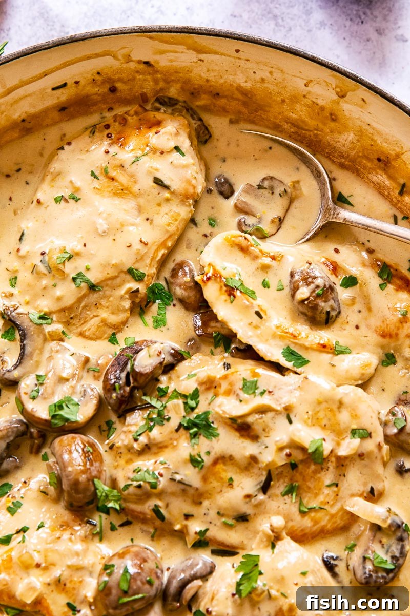 Close-up of a chicken breast half submerged in a rich garlic mushroom sauce, with fresh herbs visible.
