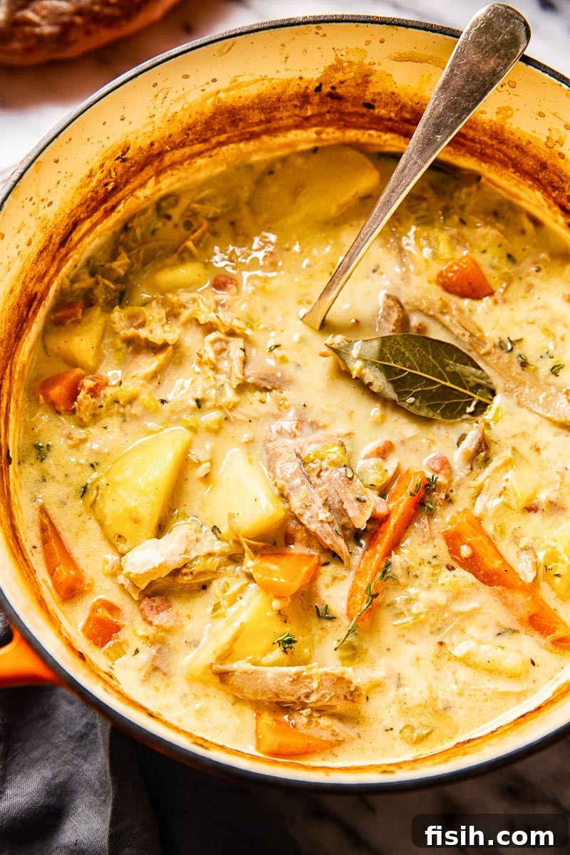creamy turkey stew with carrots and potatoes in a soup pot, garnished with fresh herbs