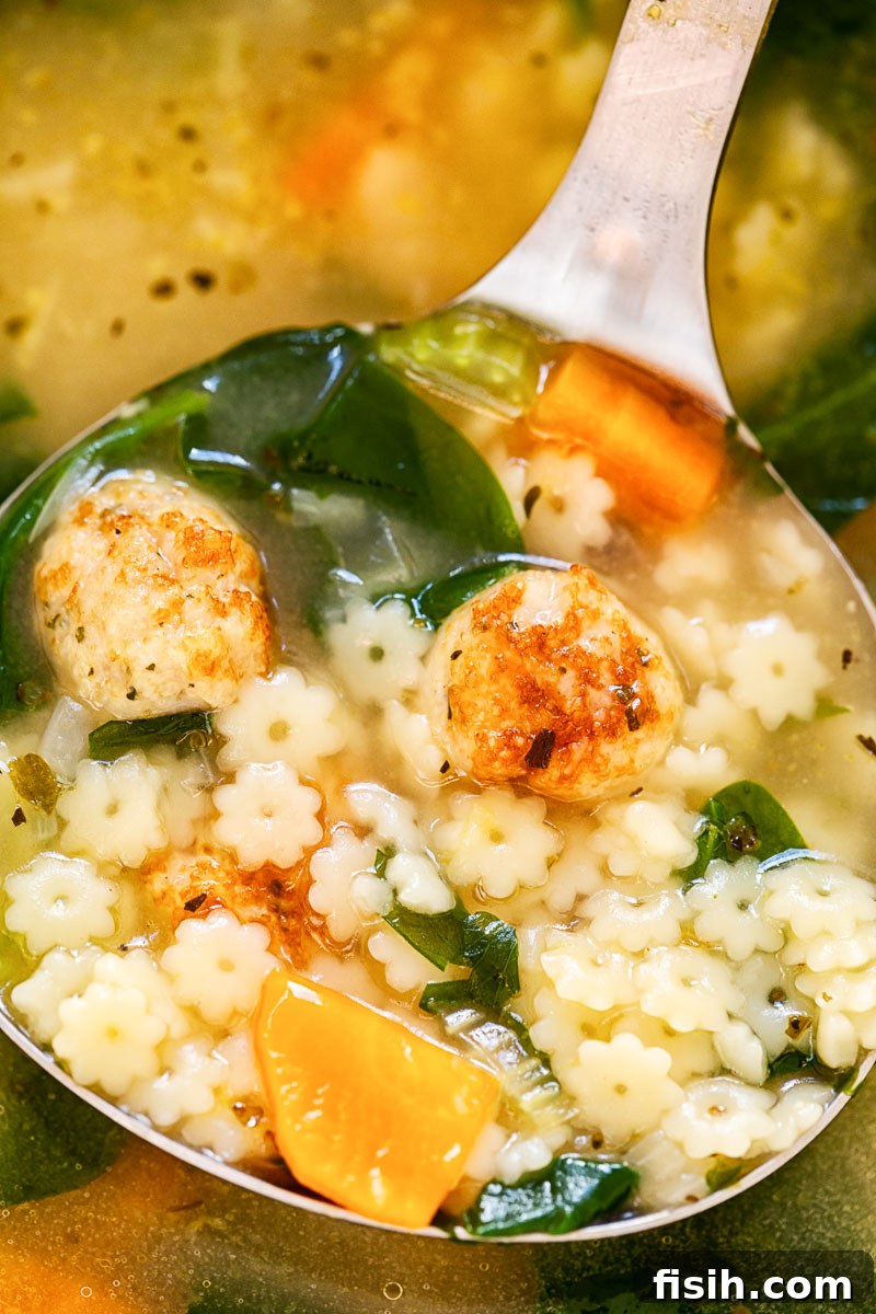 A close-up shot of Italian Wedding Soup being served with a ladle, showcasing the rich broth, small meatballs, and leafy greens.