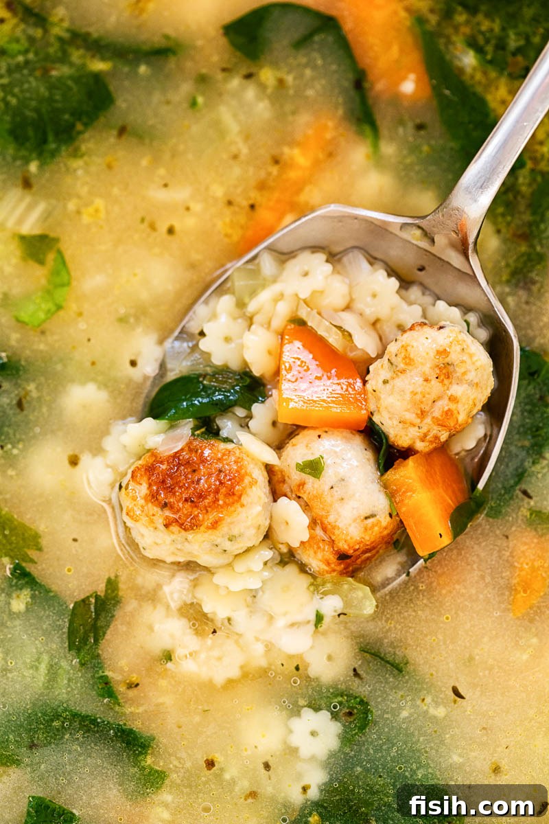 A close-up view of a large pot filled with simmering Italian Wedding Soup, showcasing the texture of the broth, meatballs, pasta, and greens.