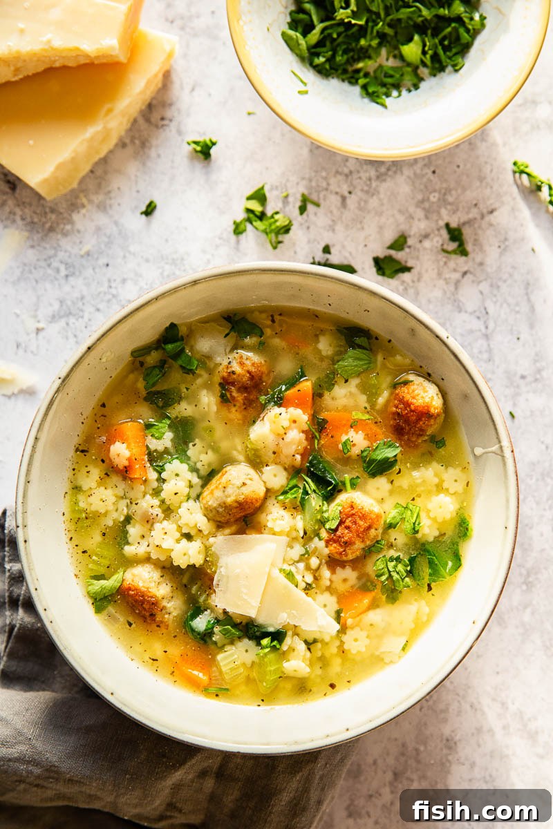 A bowl of Italian Wedding Soup garnished with fresh chopped parsley and shaved Parmesan cheese, ready to be enjoyed.