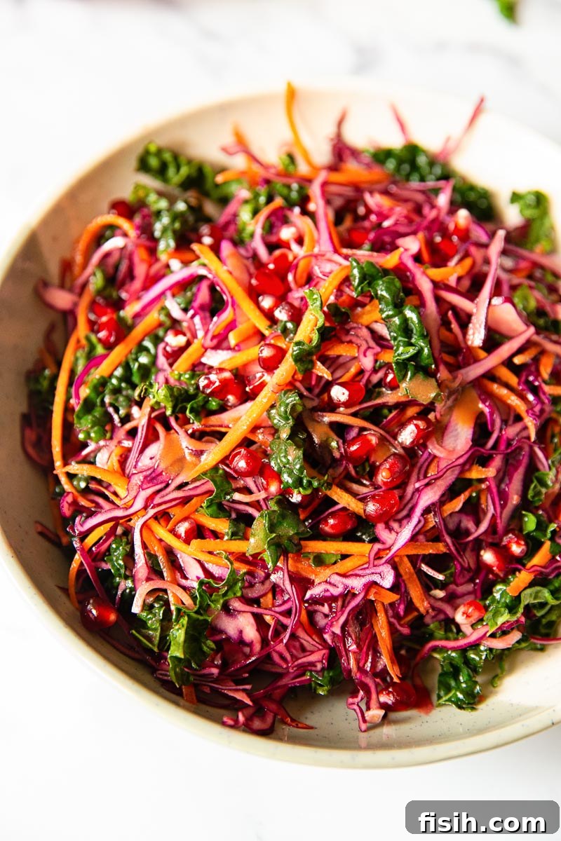 A vibrant winter salad with thinly sliced red cabbage, fresh kale, bright red pomegranate seeds, and grated carrots, dressed with a zesty vinaigrette, presented in a stylish serving bowl.