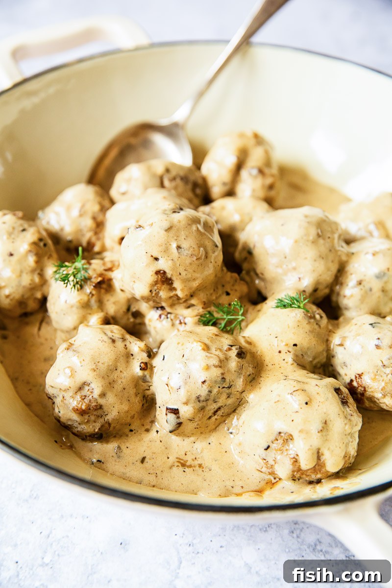 Juicy Swedish meatballs in creamy sauce shown in a white pan, ready to be served.
