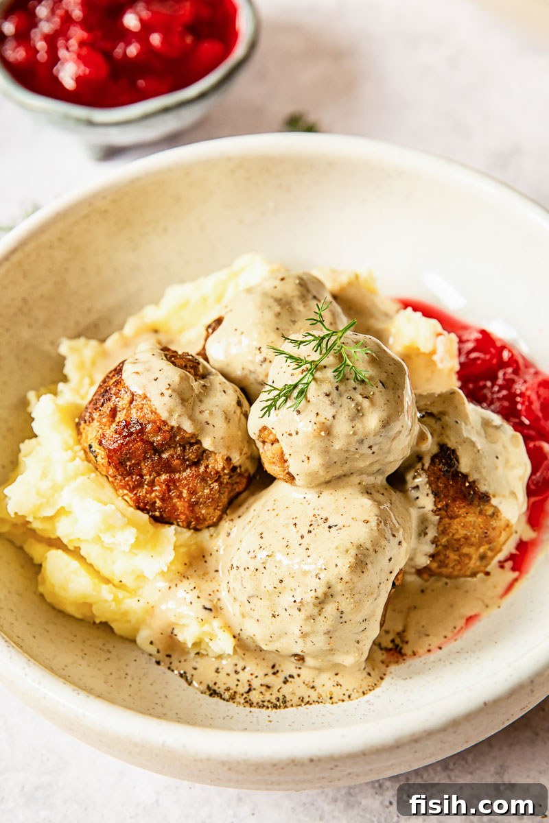 Swedish meatballs in creamy sauce served over a bed of mashed potatoes, garnished with fresh herbs.