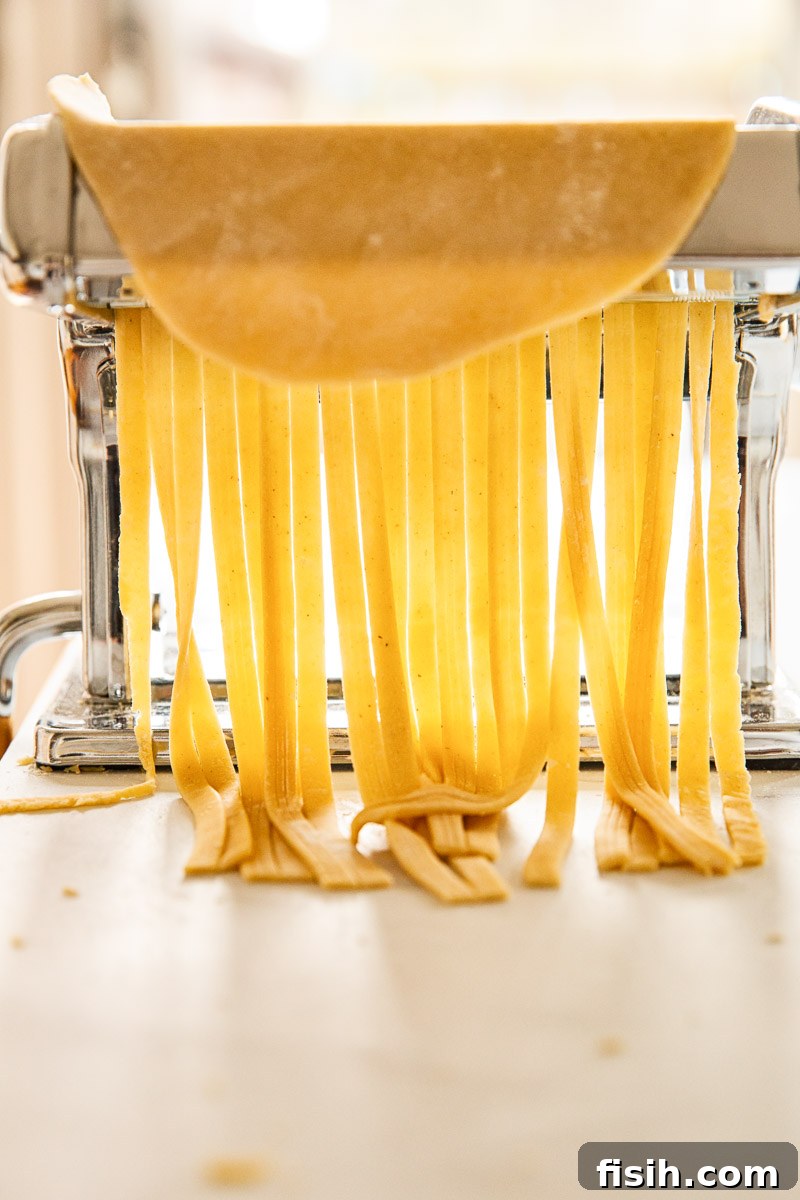 Perfect Fresh Pasta from Scratch 6 A sheet of fresh pasta dough being fed into a pasta machine to be cut into fettuccine