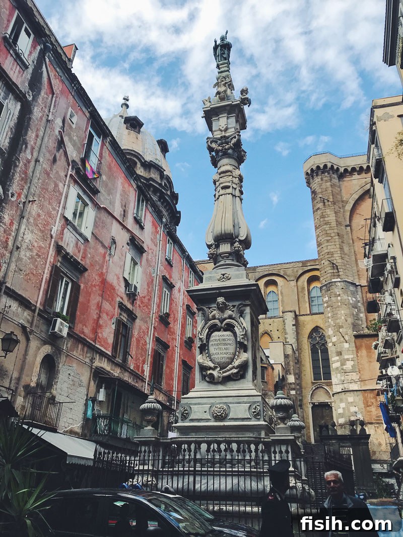 A lively town square in Naples, Italy, with historic buildings, a prominent statue or monument, and people enjoying the vibrant city life under a clear sky.