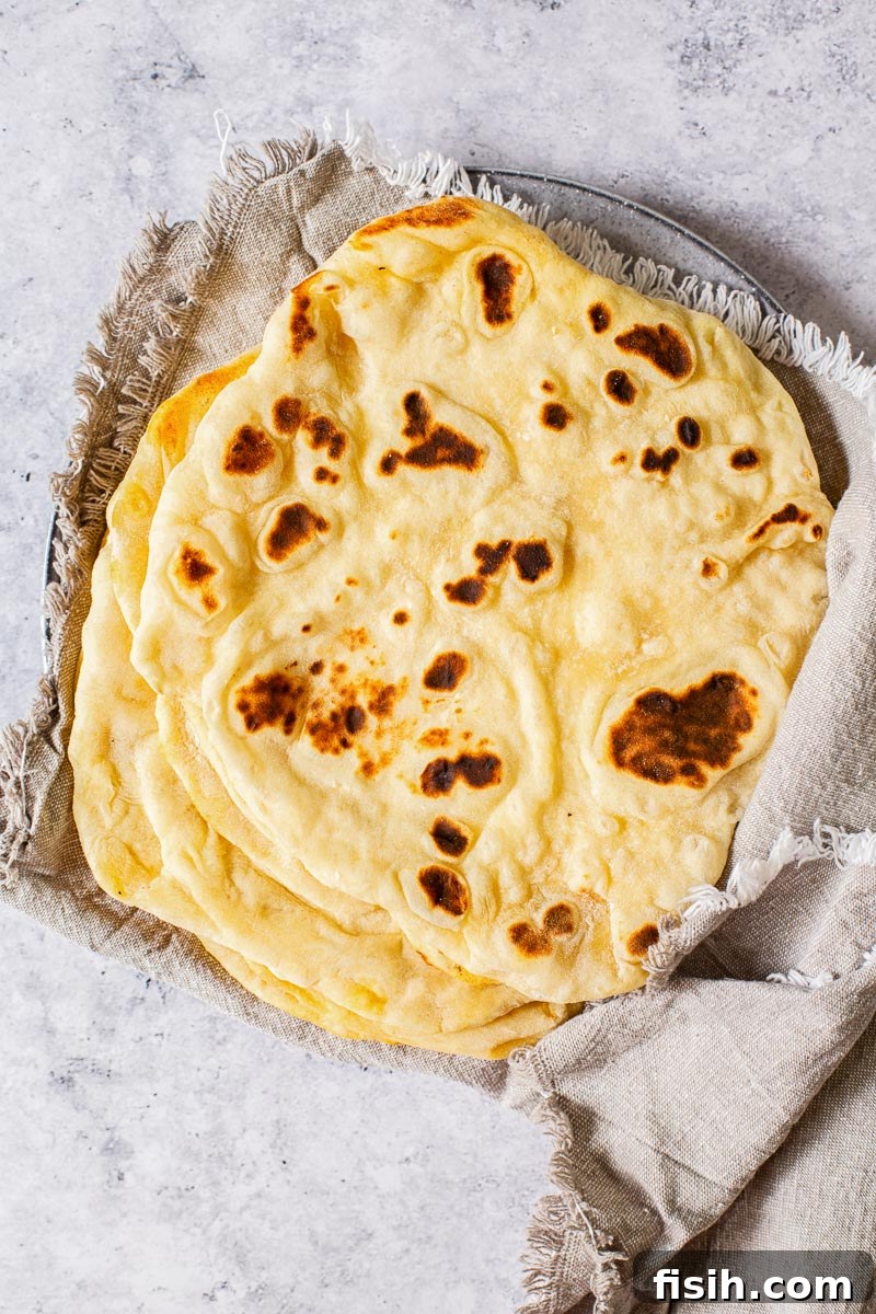 Stack of fluffy pita breads wrapped in a grey cloth napkin, ready to be served.