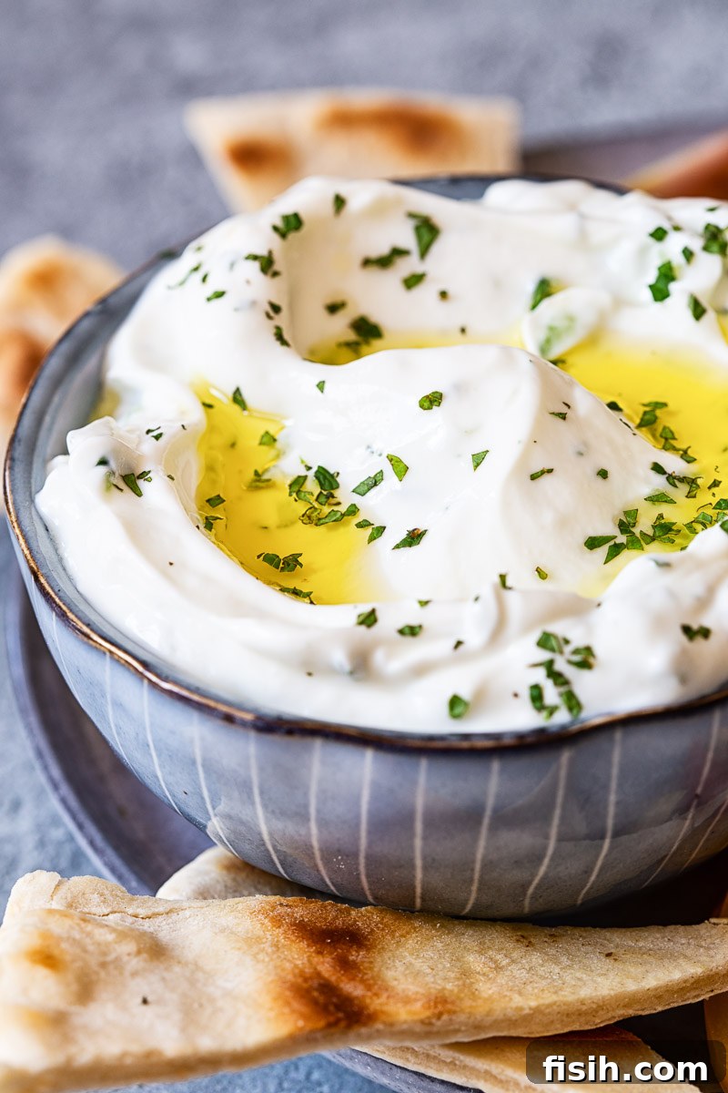 Authentic Greek Tzatziki Recipe 2 Tzatziki sauce in a blue bowl, surrounded by warm pita bread, ready for dipping.