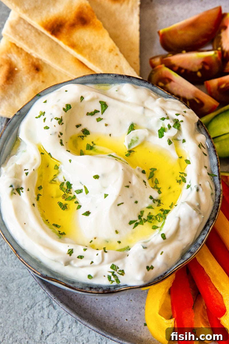 Authentic Greek Tzatziki Recipe 3 Creamy yogurt and cucumber dip garnished with fresh mint, served on a platter with pita bread and colorful chopped vegetables.