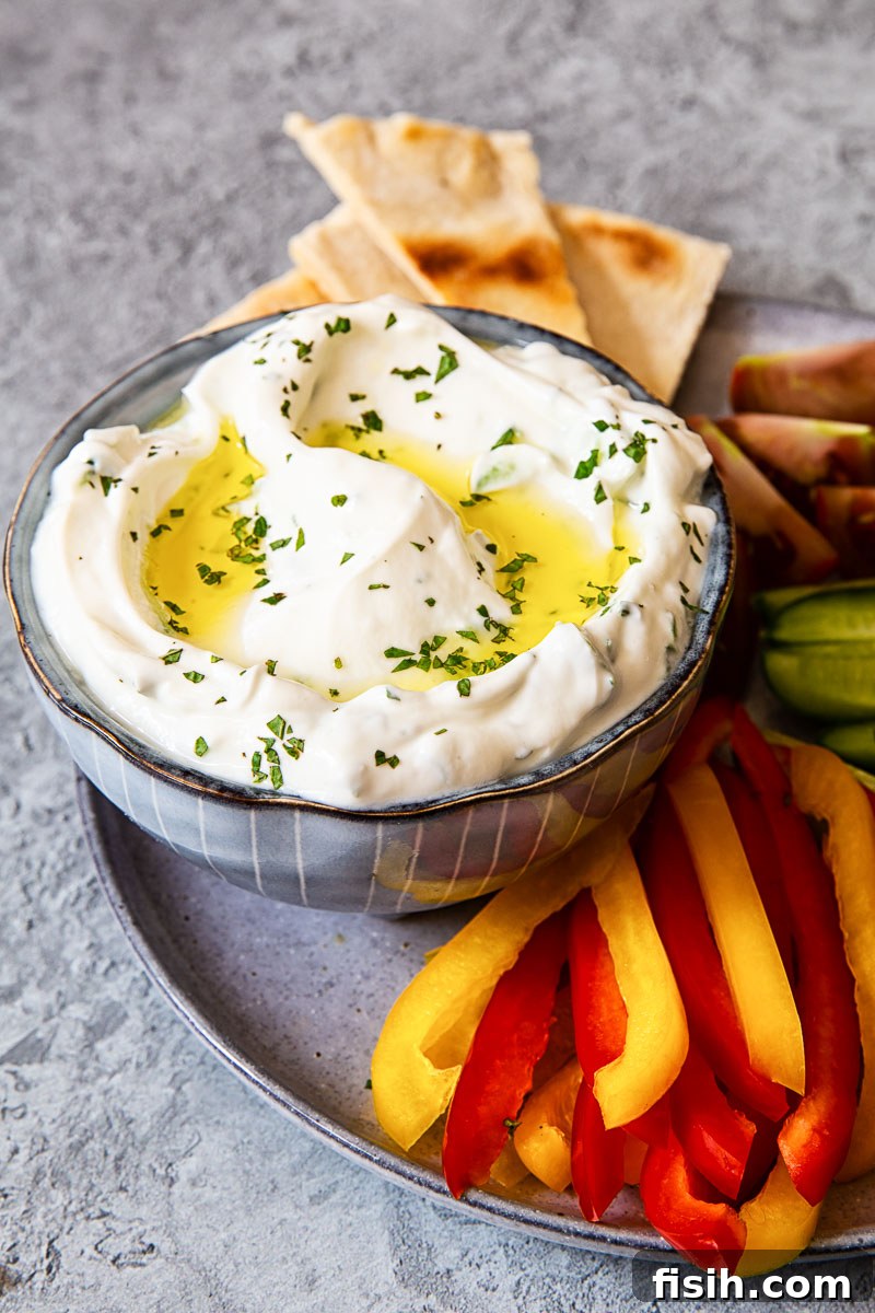 Authentic Greek Tzatziki Recipe 5 A serving of Greek tzatziki in a blue bowl, accompanied by vibrant red and yellow bell pepper sticks and warm pita bread.