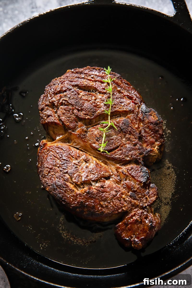 A perfectly cooked ribeye steak, still sizzling, resting in a cast iron pan.