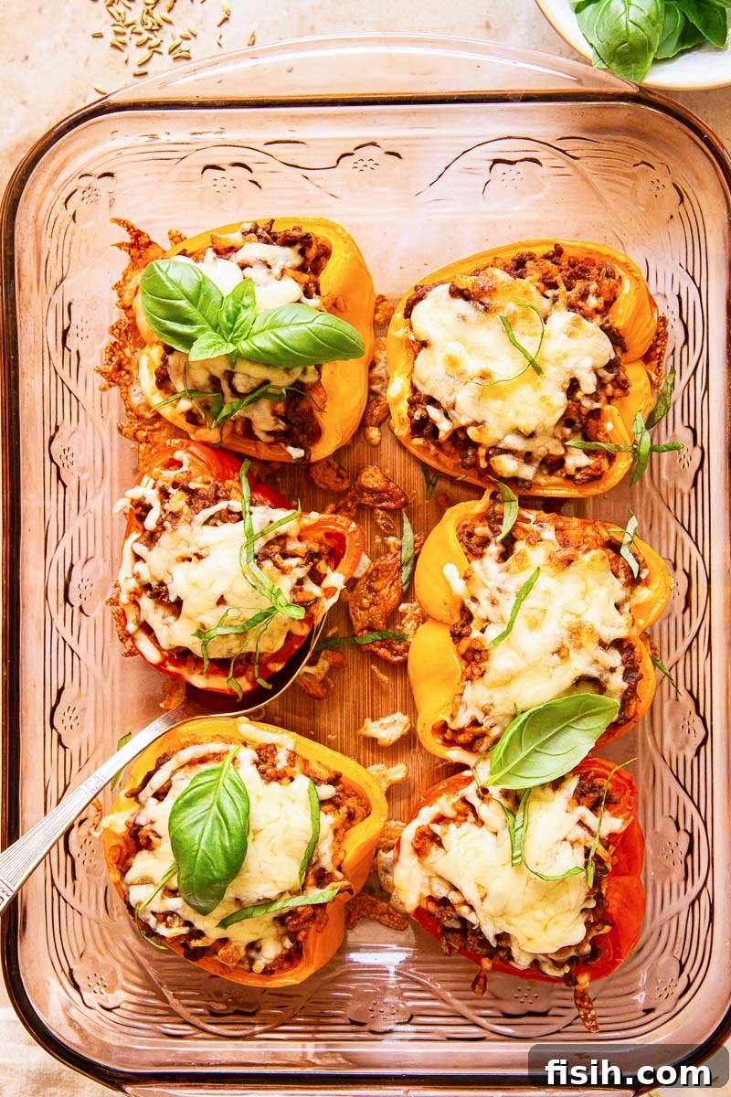 Vibrant bell peppers filled with cheesy beef risotto, garnished with fresh basil and melted mozzarella, served in a baking dish.