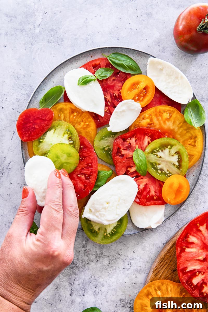Caprese Dream: Juicy Tomatoes, Aromatic Basil, Creamy Mozzarella 4 a thick slice of creamy mozzarella being carefully placed onto a Caprese salad