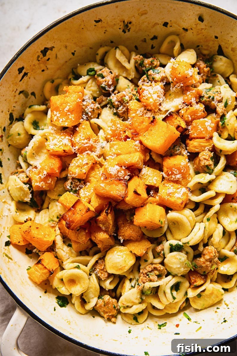 A close-up shot of butternut squash pieces nestled within orecchiette pasta, chorizo, and spinach in a creamy Parmesan sauce.