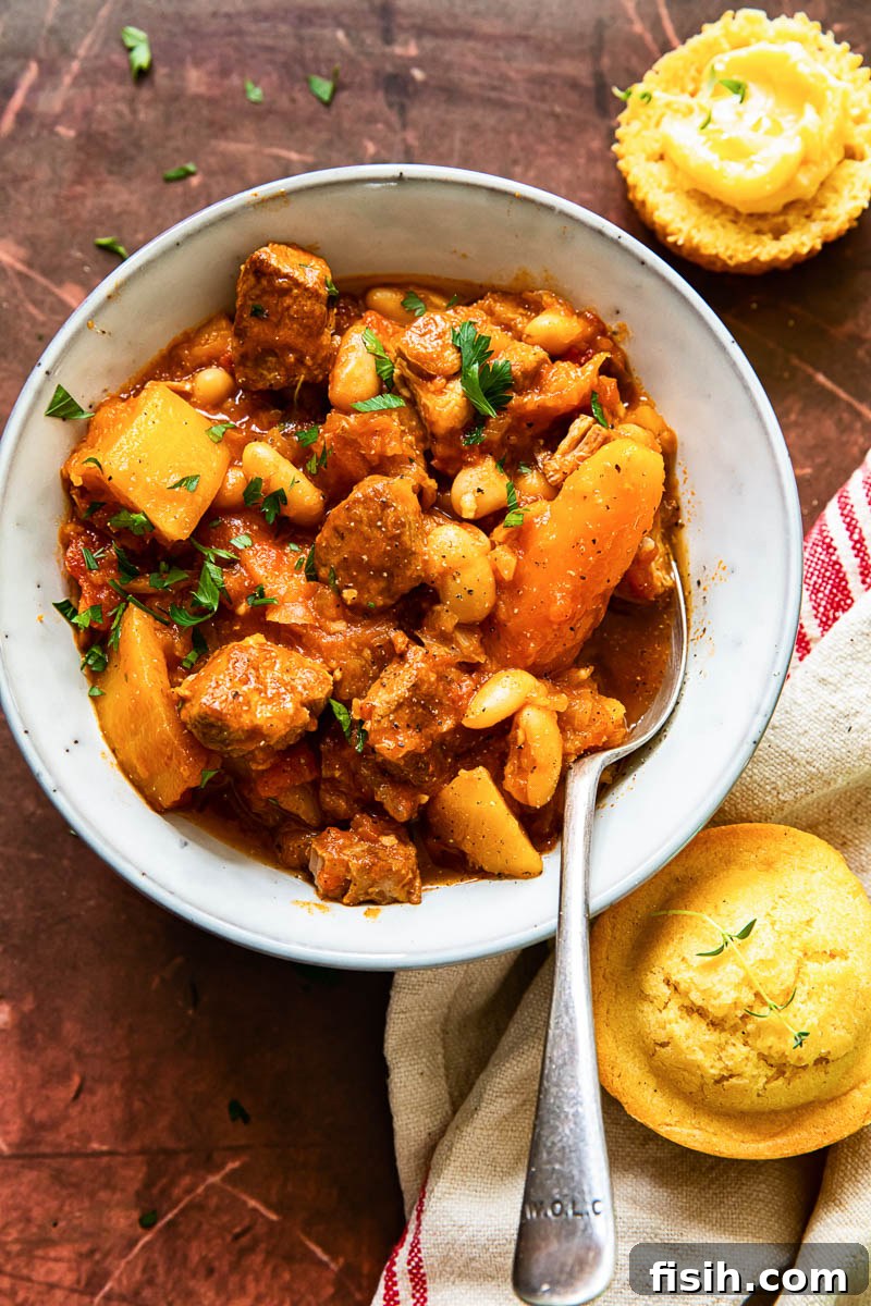 A delicious serving of pork stew with carrots and butternut squash in a bowl, accompanied by golden cornbread muffins, ready to be enjoyed.