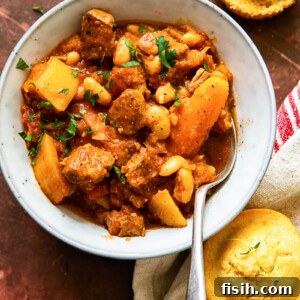 A delicious serving of pork stew with carrots and butternut squash in a bowl, accompanied by golden cornbread muffins.