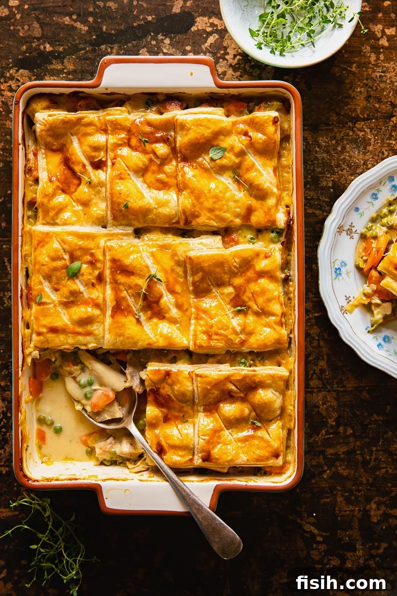Close-up top-down view of a turkey pot pie with golden puff pastry on a rustic brown background