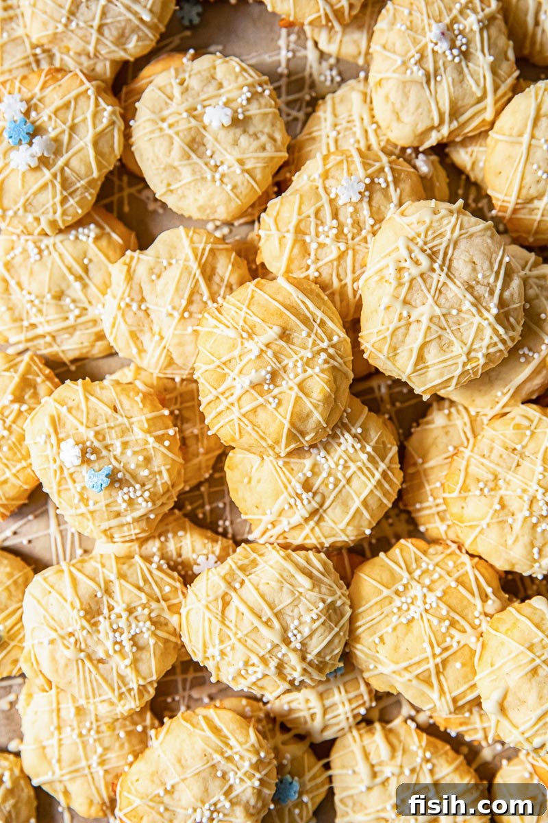 An overhead view of numerous lemon ricotta cookies artfully arranged, each glistening with white chocolate and delicate sprinkles.