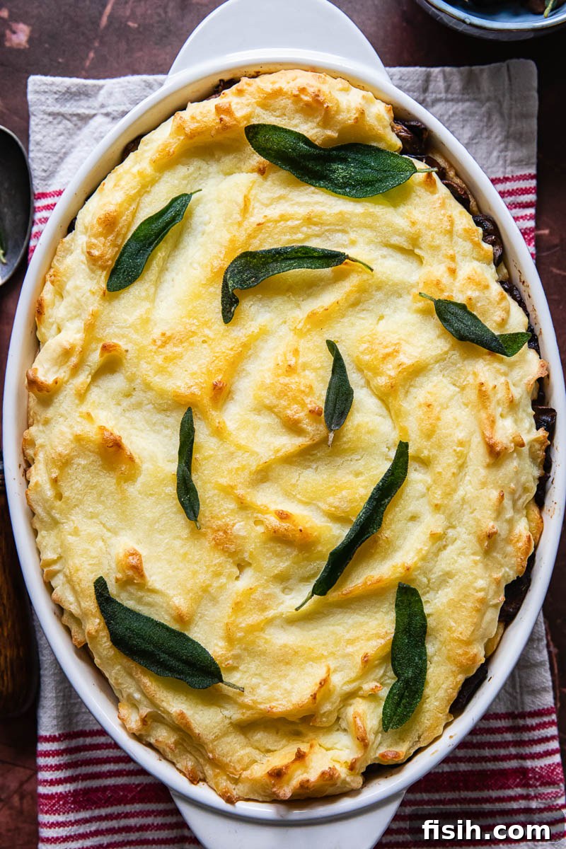 Creamy Potato Bake with Caramelized Onions and Mushrooms 2 Mashed potato casserole topped with fried sage leaves, ready for serving on a holiday table