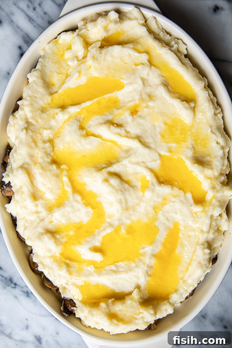Creamy Potato Bake with Caramelized Onions and Mushrooms 5 Unbaked mashed potatoes in a casserole dish with melted butter drizzled on top, ready for the oven