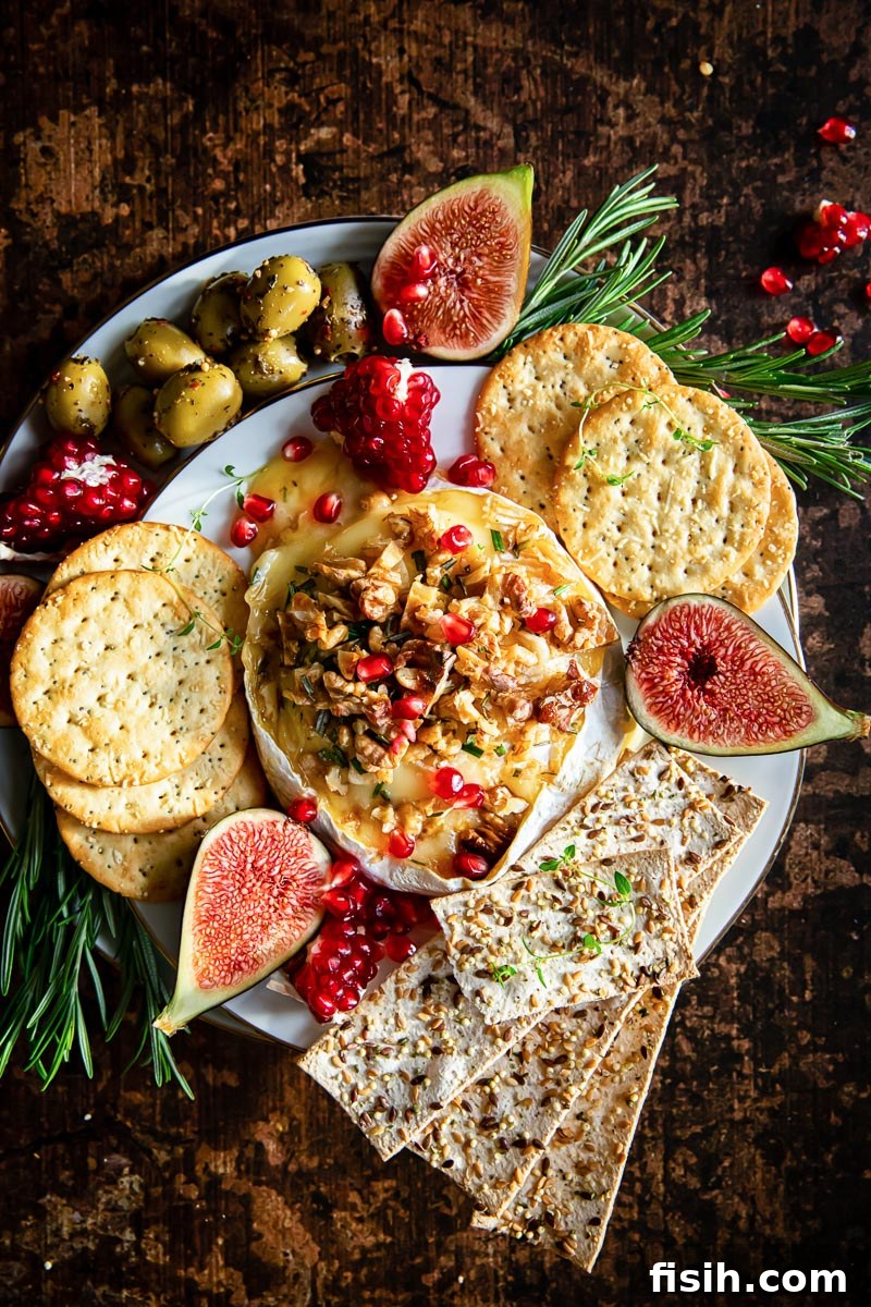 Top down view of baked brie surrounded by crackers, olives, figs and pomegranate seeds