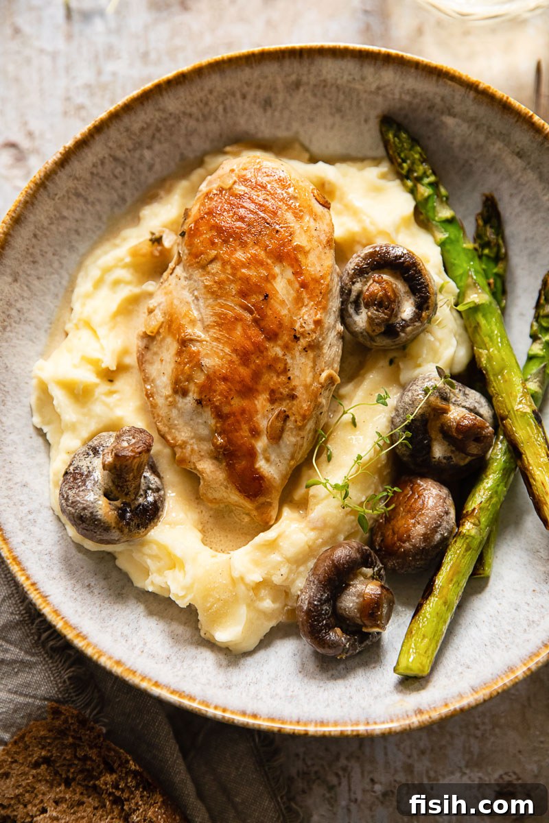 Chicken Supreme in Velvety White Wine Mushroom Cream 3 Chicken breast and mushrooms elegantly plated on a bed of mashed potatoes with fresh asparagus on the side, highlighting the rich cream sauce.