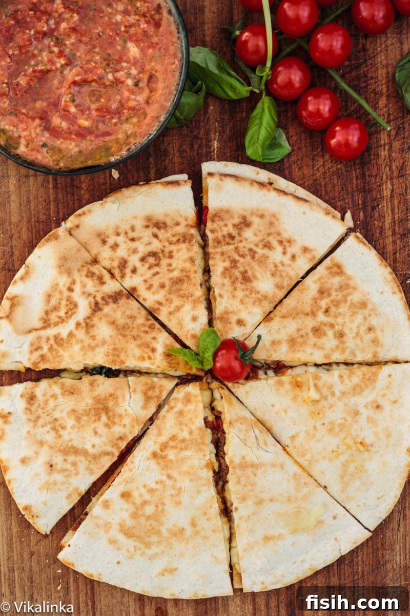 Top-down view of an Italian Beef Quesadilla cut into wedges, served with a vibrant tomato basil salsa on the side.