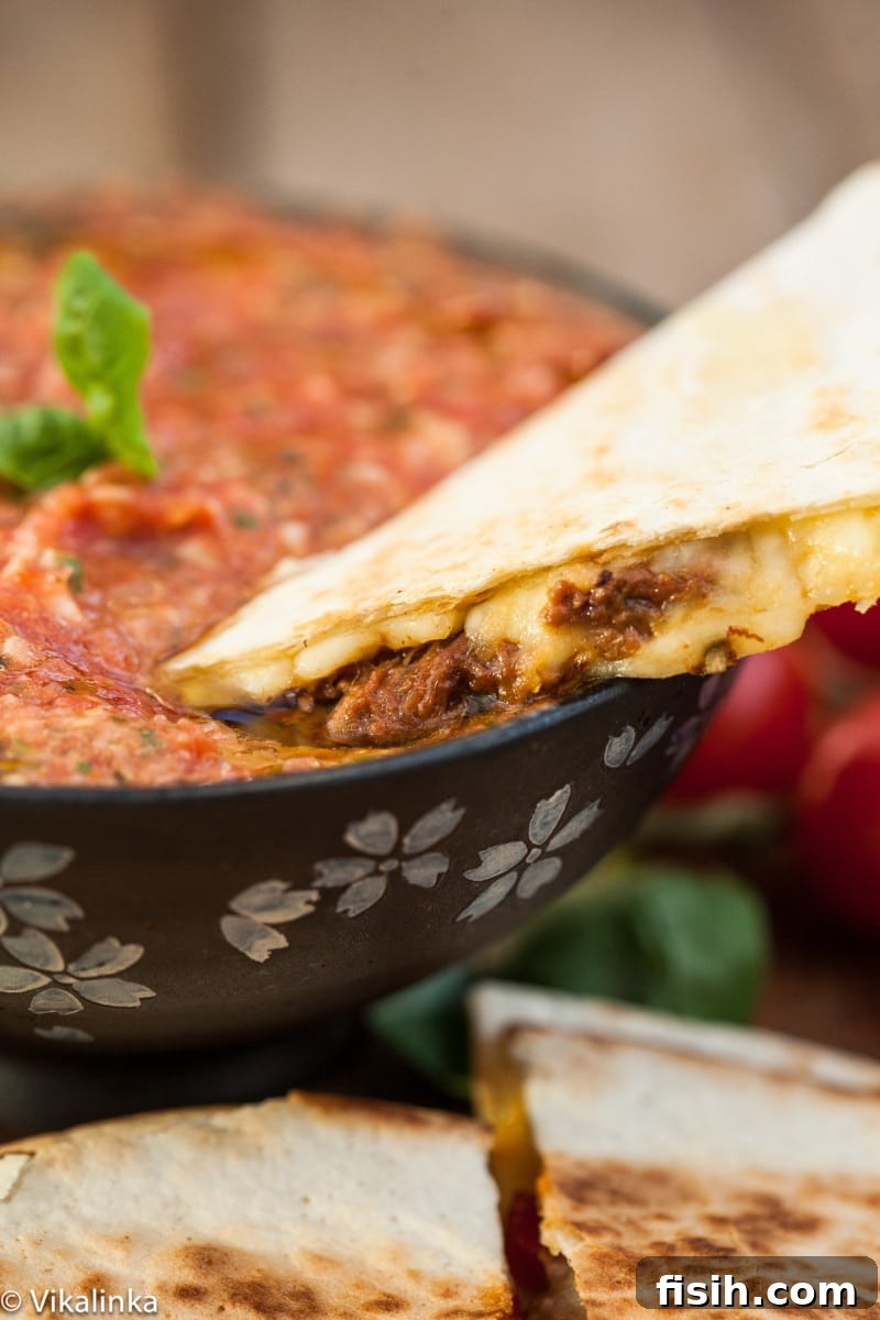A wedge of Italian Beef Quesadilla being dipped into a bowl of fresh tomato basil salsa, highlighting its deliciousness.