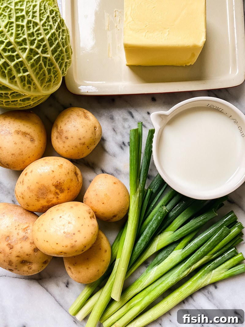 Ingredients for Irish colcannon laid out on a marble surface: potatoes, fresh green onions, a pat of butter, milk, and crinkled Savoy cabbage leaves.