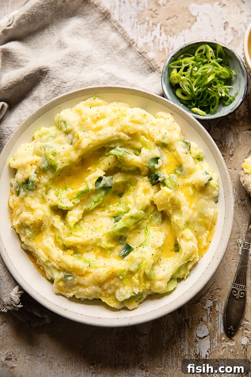 Top-down view of Irish Colcannon in a cream-colored bowl, accompanied by a small bowl of sliced green onions and a gray napkin.