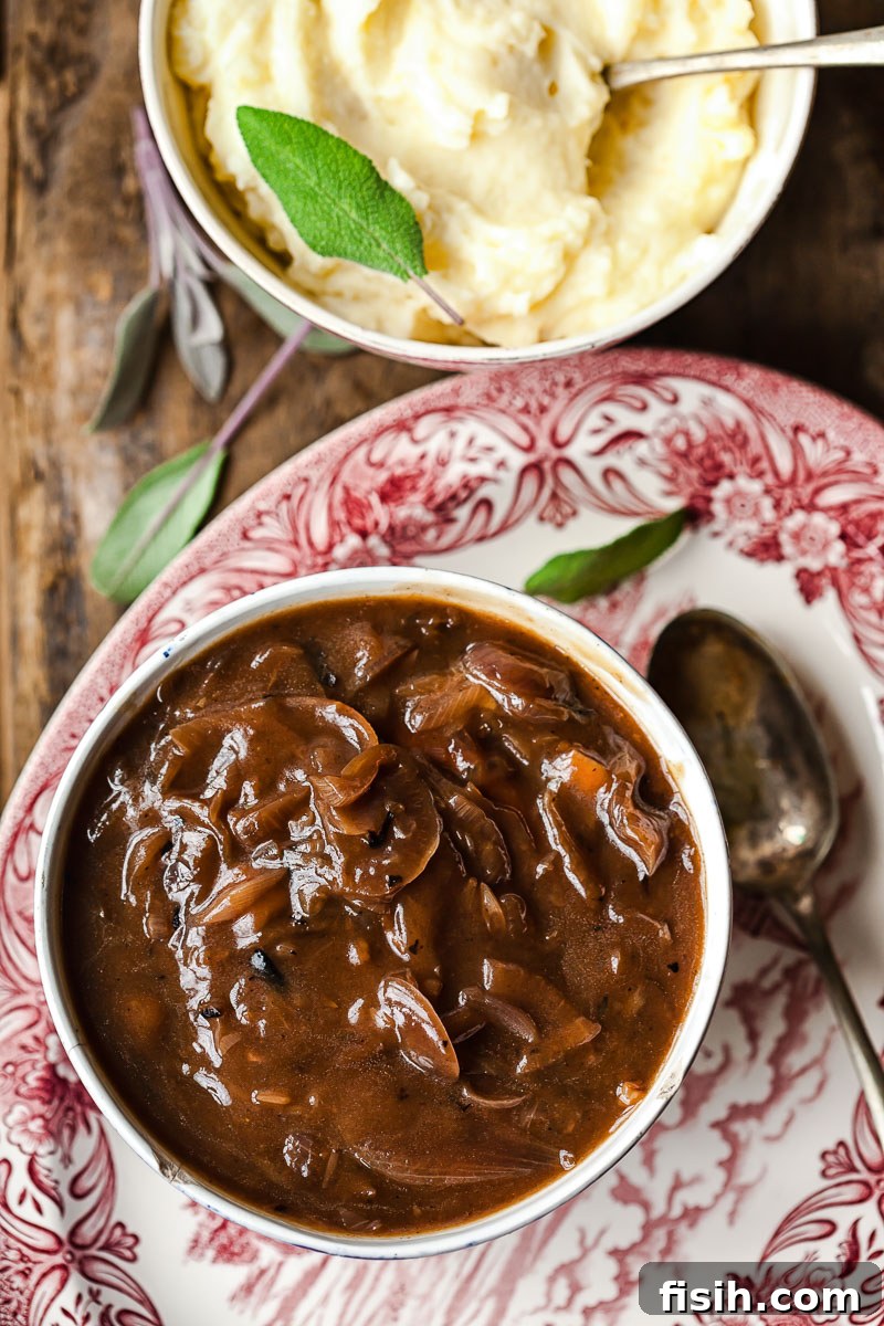 Top-down view of red onion gravy in a bowl, alongside mashed potatoes garnished with fresh sage leaves.