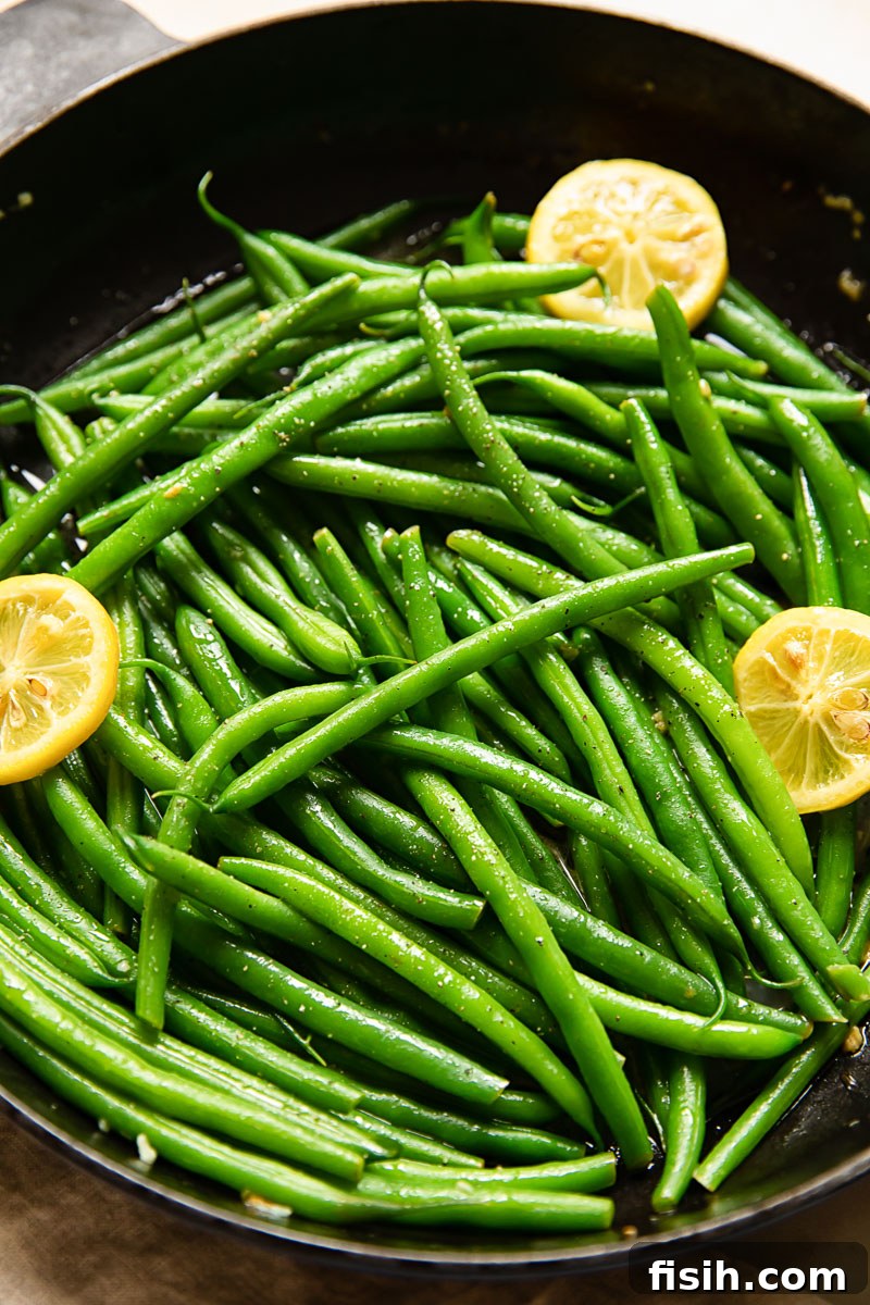 Bright Lemon-Garlic Parmesan Green Beans 3 Freshly cooked green beans tossed with lemon slices and garlic in a rustic cast iron pan, ready to be served as a flavorful side.