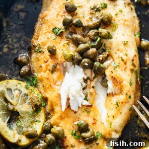 Close-up of perfectly cooked sole fillet generously topped with capers and fresh lemon slices in a cast iron pan.