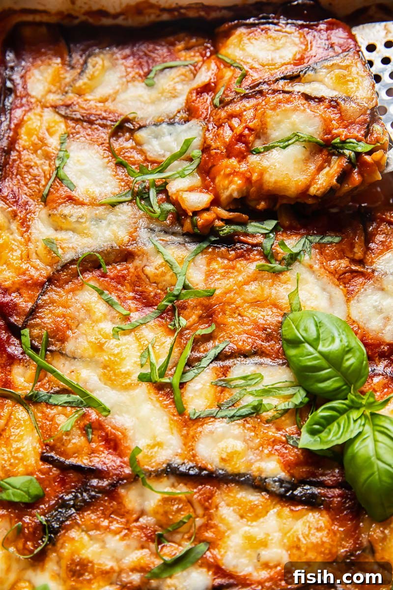 Guilt-Free Eggplant Parmigiana 4 A close-up shot of baked Eggplant Parmigiana, still in the pan, with a perfect slice being carefully lifted out, showcasing the melted cheese and layered texture.