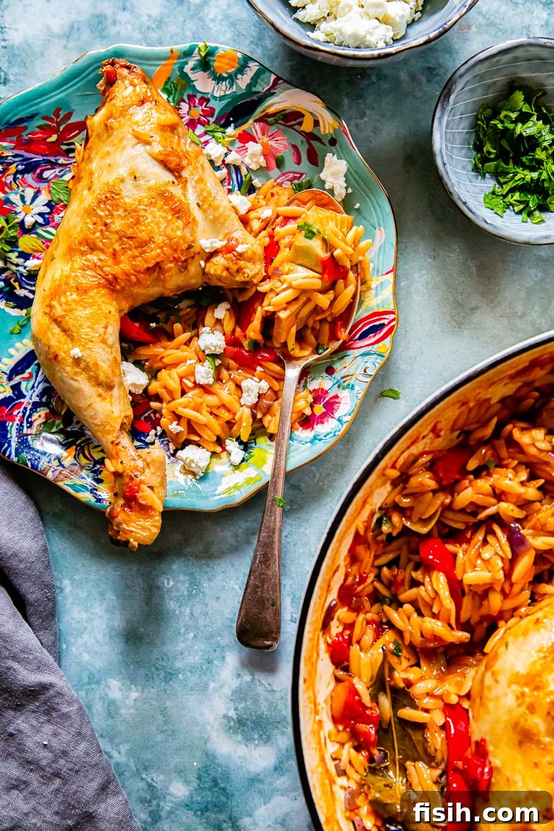 A serving of Greek chicken and orzo on a blue plate, with small bowls of feta and parsley and the main pan in the background.