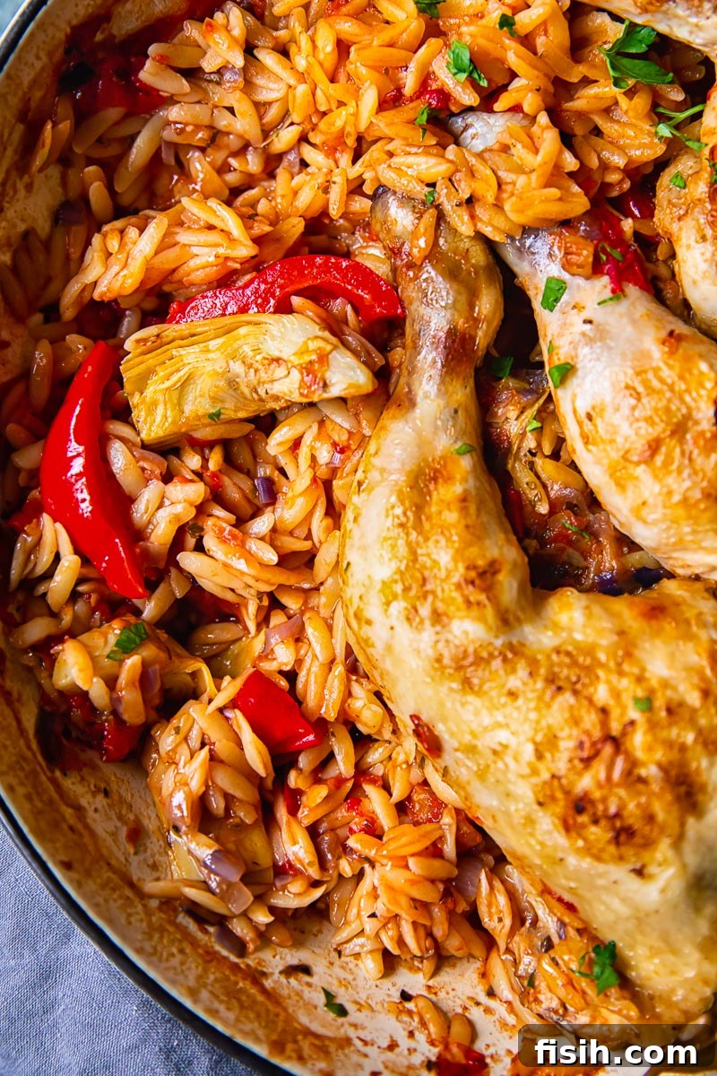 An overhead view of the Greek chicken and orzo dish in the pan, garnished with fresh herbs.