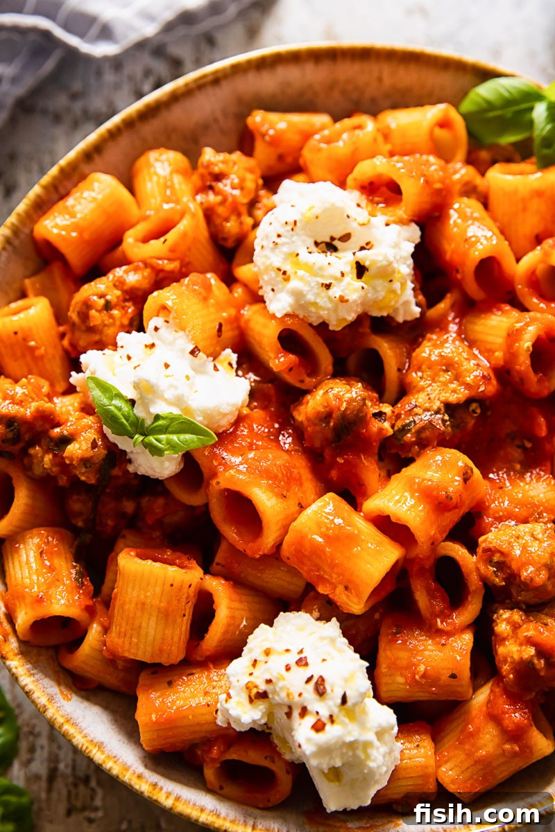 Zesty Sausage Pasta with Creamy Ricotta 2 Top-down view of rigatoni pasta with spicy sausage in tomato sauce, generously topped with creamy ricotta.