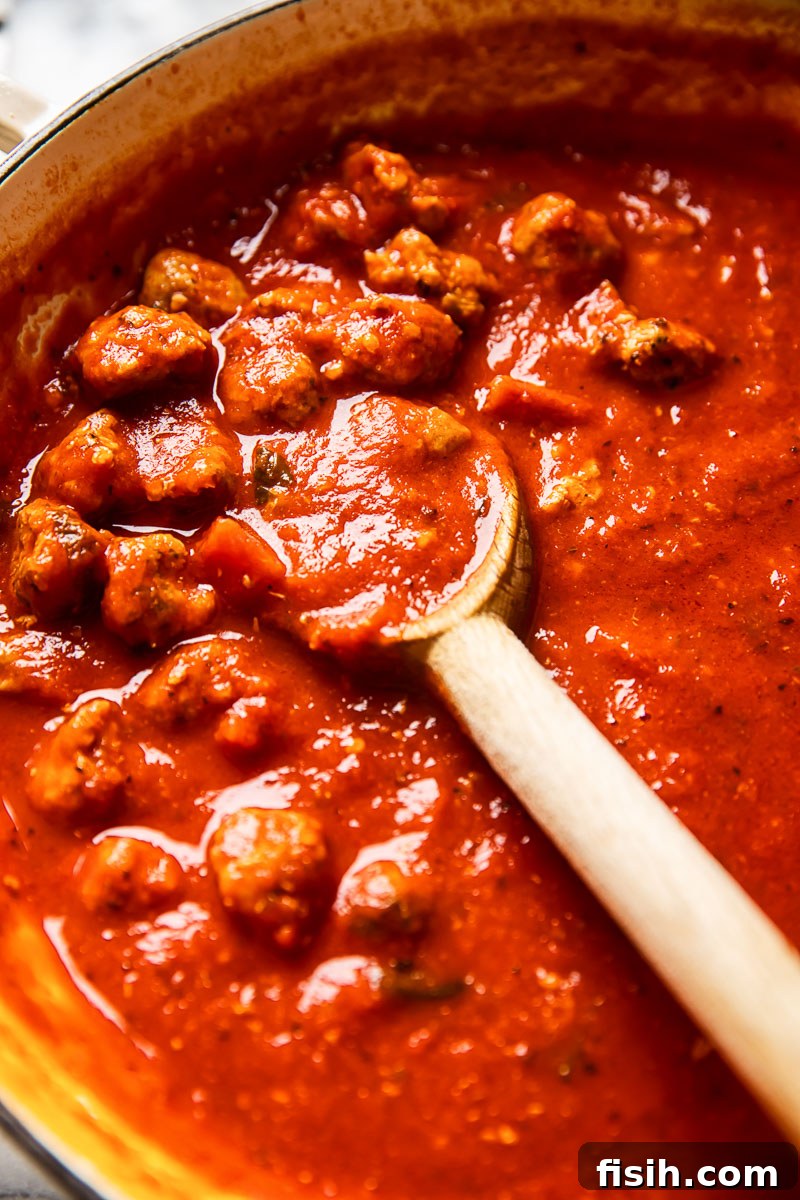 Zesty Sausage Pasta with Creamy Ricotta 3 Sausage pasta sauce simmering in a pan with a wooden spoon, showcasing rich red colors.