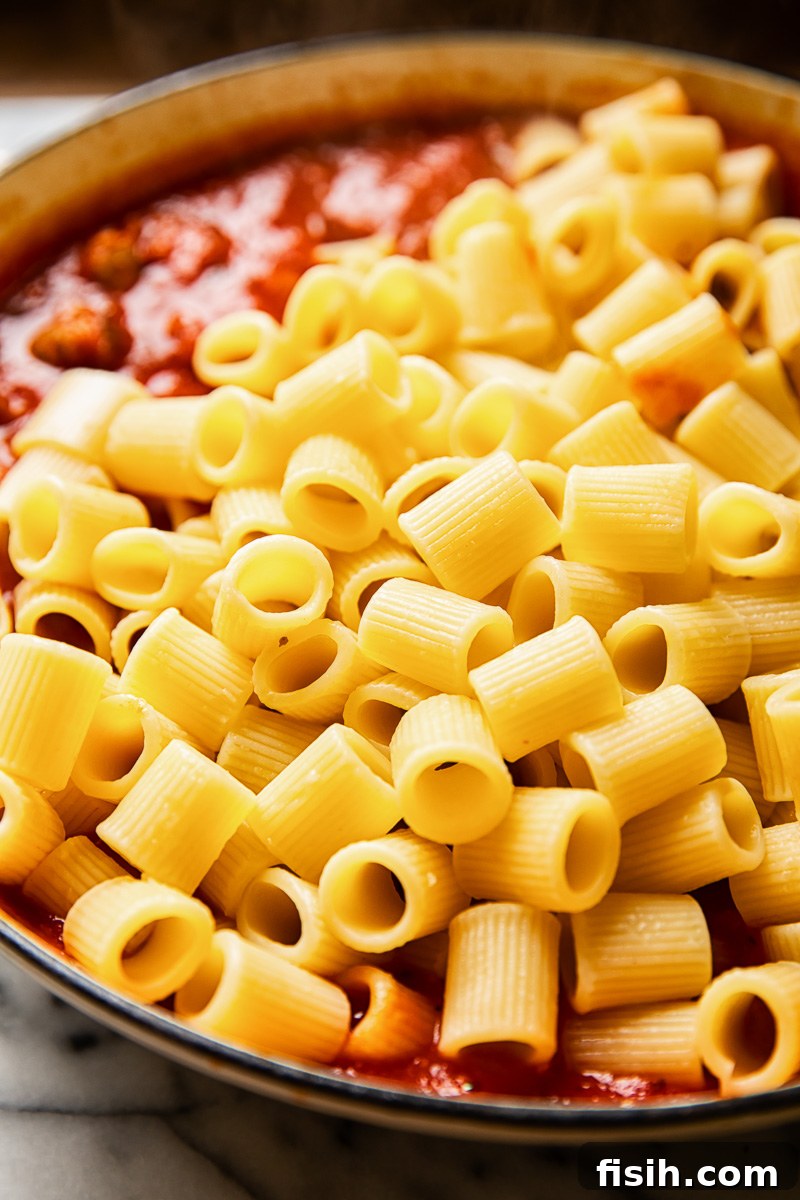 Zesty Sausage Pasta with Creamy Ricotta 4 Cooked rigatoni pasta resting on a bed of rich, spicy sausage tomato sauce in a large pan.