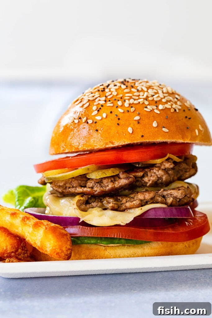 A delicious smash burger from a side view, featuring perfectly melted cheese, sliced tomatoes, crisp lettuce, and pickles
