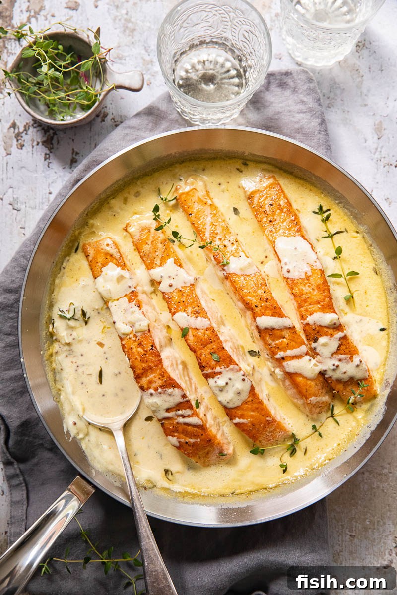 Pan-Seared Salmon with Tangy Creamy Mustard 6 Top-down view of pan-seared salmon pieces in creamy sauce, with glasses and herbs on the table.