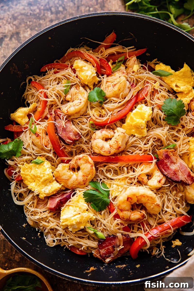 Top down view of colorful Singapore Noodles in a wok, garnished with fresh herbs