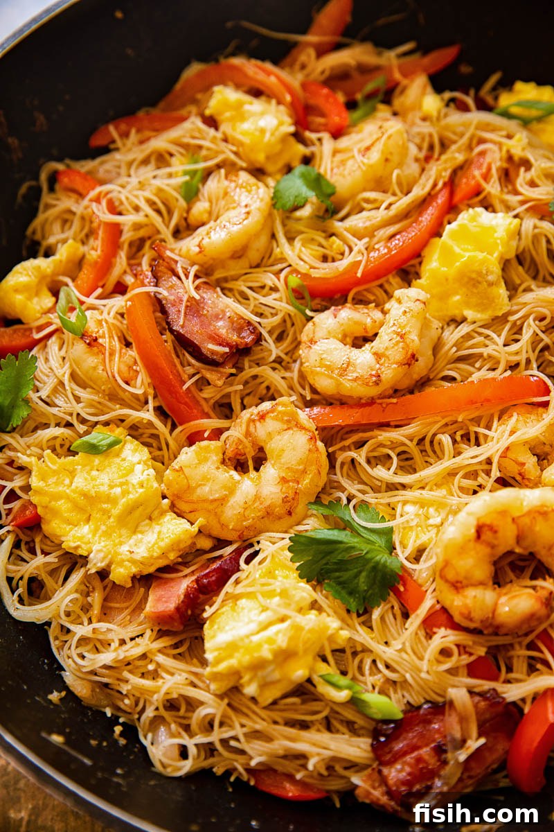 A generous serving of Singapore Noodles ready to eat in a large wok, garnished with fresh herbs