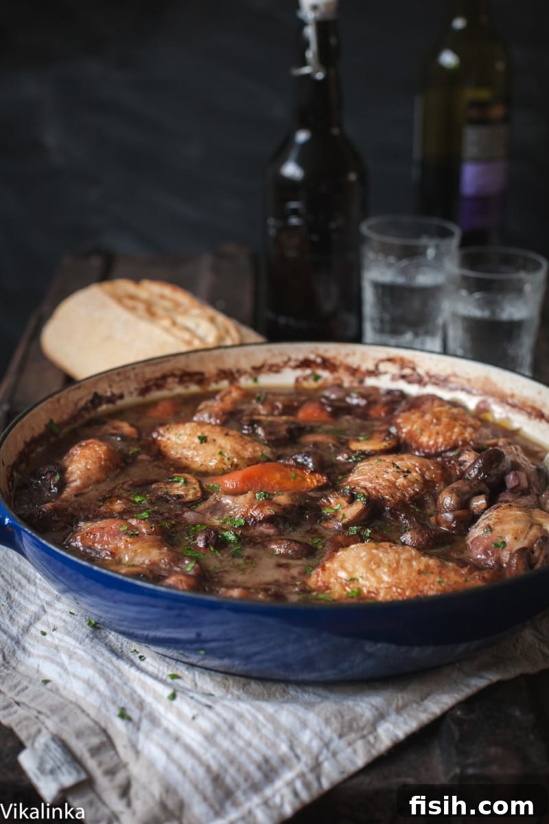Chicken coq au vin with red wine and glasses in background