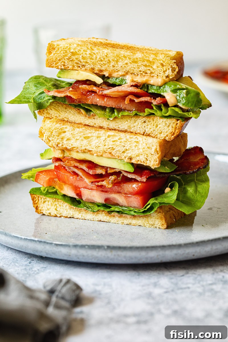 A Maple BLT sandwich cut cleanly in half, revealing its perfectly stacked layers of maple bacon, fresh lettuce, ripe tomato, creamy avocado, and smoky chipotle aioli.